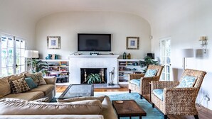 A living room with a fireplace, a television, and wicker furniture. - La Jolla Shores Oceanview Retreat (San Diego)