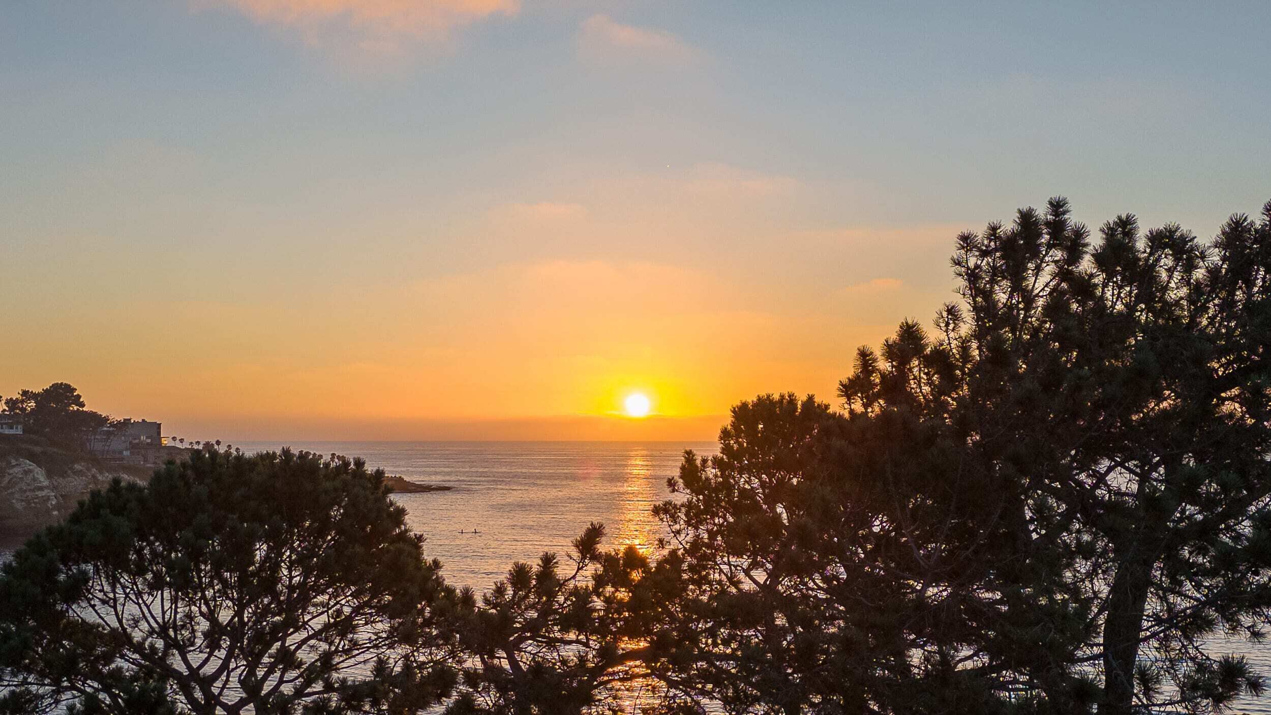 Atardecer sobre una zona costera con árboles en primer plano.