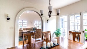 A dining area with a wooden table set for four, a chandelier, and a view into a living room with a sofa and chairs. - La Jolla Shores Oceanview Retreat (San Diego)