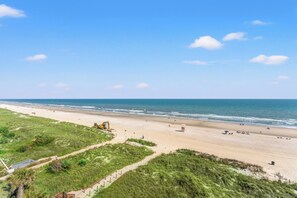 A beach with a clear sky, a sandy shore, and a grassy area with a path.