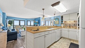 A modern kitchen with white cabinets, a central island, and a view of the ocean. - Crescent Towers II 608 - Oceanfront 2 BR Condo (North Myrtle Beach)
