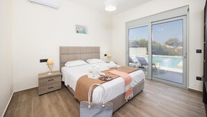 Un dormitorio con cama, mesitas de noche, lámpara, ventana y vista a una piscina y zona exterior.