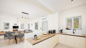 Una cocina moderna con una isla central, un comedor con mesa y sillas, y una sala de estar con sofá y televisor.