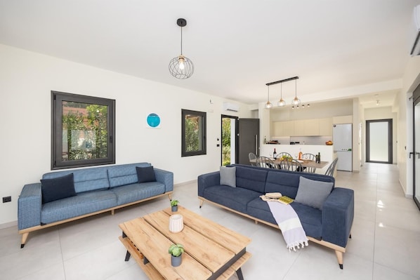 Un salon moderne avec deux canapés, une table basse en bois et une cuisine en arrière-plan.