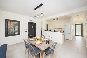 Eine moderne Küche mit weißen Schränken, einem eingebauten Backofen und einem Essbereich mit einem Holztisch und Stühlen.