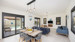 A modern living space with a dining area, sofa, and TV. - Villa Petra - Two Bedroom Villa, Sleeps 4 (Afrato)