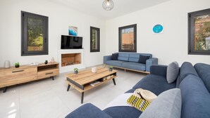 A modern living room with a fireplace, a sofa, a coffee table, and a TV mounted on the wall. - Villa Petra - Two Bedroom Villa, Sleeps 4 (Afrato)