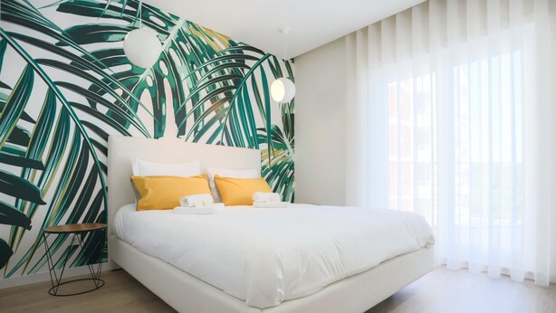 Un dormitorio moderno con una cama grande, ropa de cama blanca y un papel tapiz con hojas tropicales.