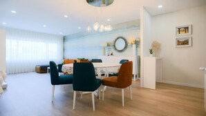Un comedor moderno con una mesa redonda, sillas color turquesa y naranja, y un armario blanco con espejo y objetos decorativos.
