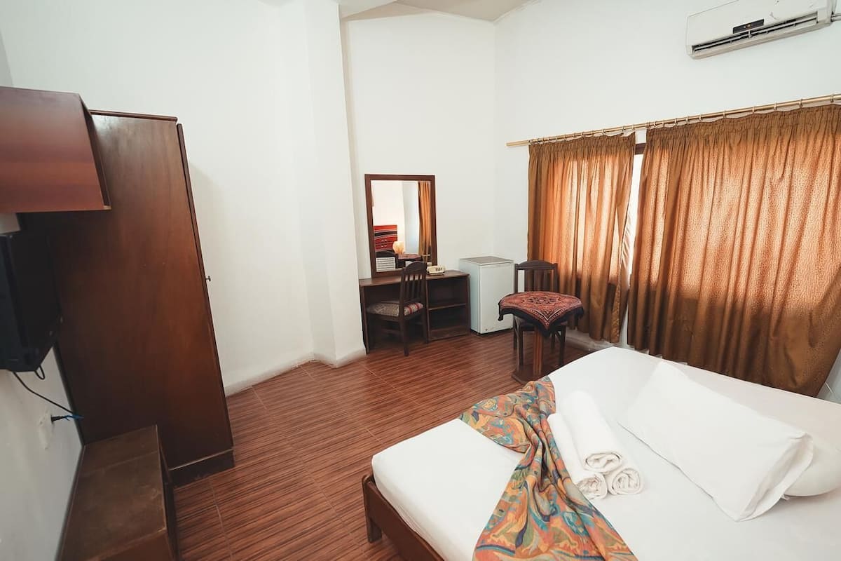 A hotel room with a bed, a desk, a chair, a wardrobe, and a mirror.