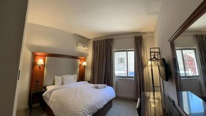 Une chambre d’hôtel avec un grand lit, un bureau, une chaise, une télévision et une fenêtre avec des rideaux.