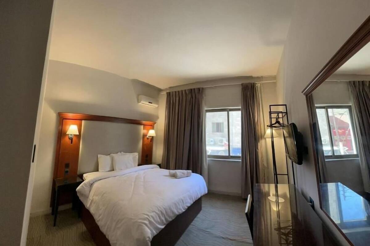 A hotel room with a large bed, a desk, a chair, a TV, and a window with curtains.