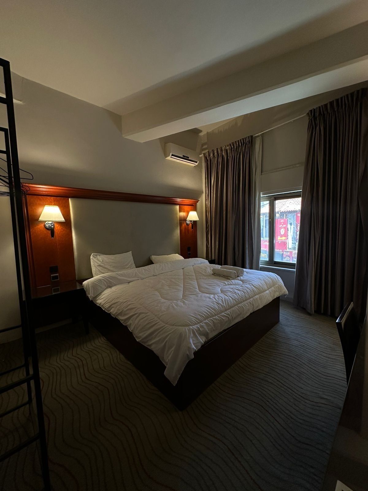 Habitación de hotel con una cama grande, dos lámparas de noche, una ventana con cortinas y un equipo de aire acondicionado.