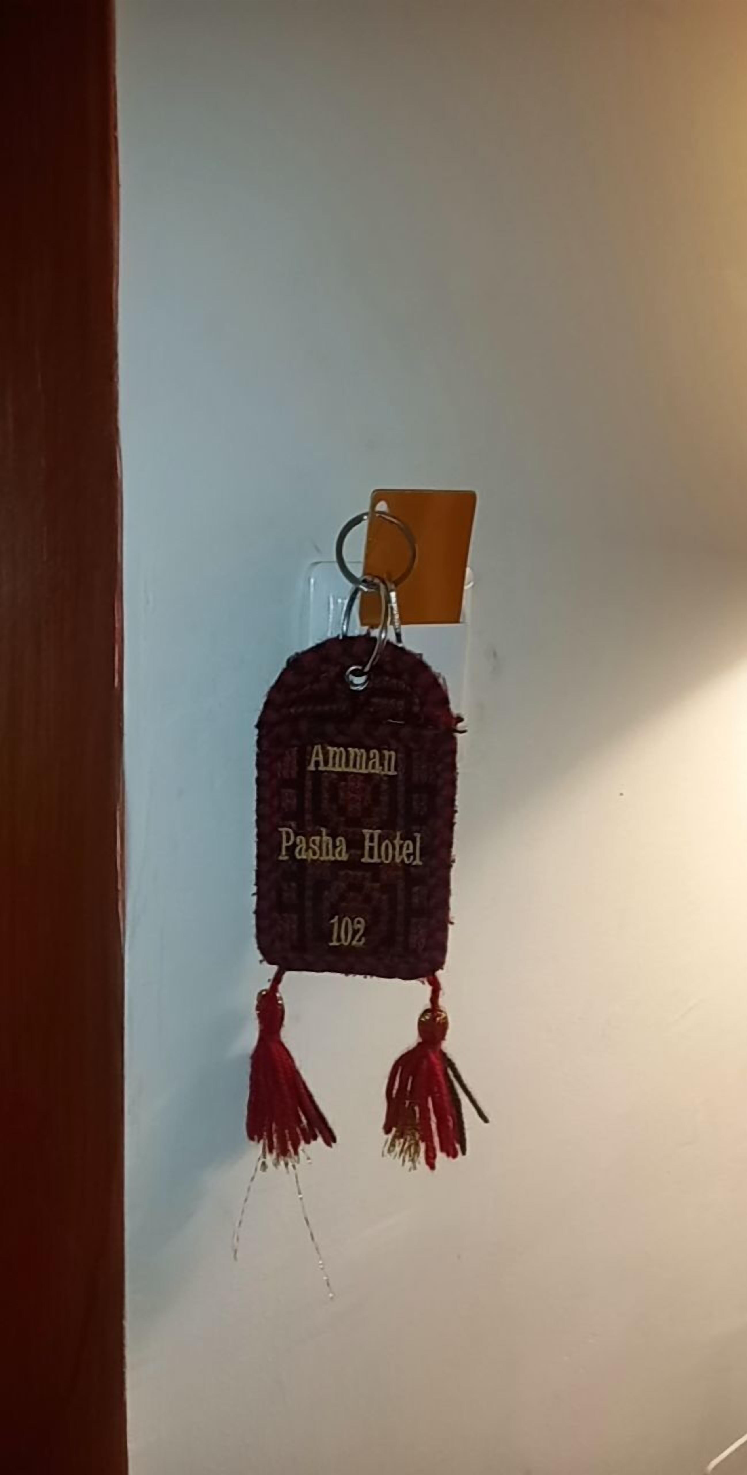 A keychain with the text "Amman Pasha Hotel 102" hanging on a wall.