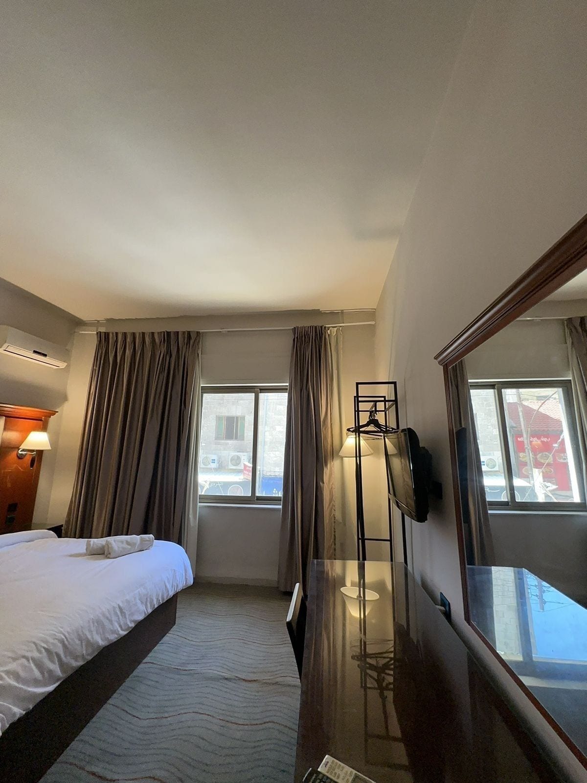 Una habitación de hotel con cama, escritorio, lámpara y un espejo grande.