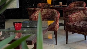 Un hall d’entrée avec des fauteuils à motifs, un comptoir de réception en marbre et une carte affichée au mur.