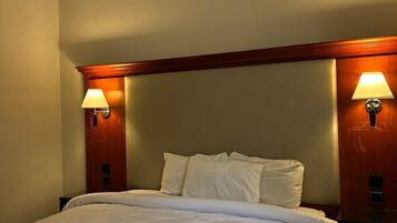 A hotel room with a large bed, two bedside lamps, an air conditioning unit, and a wooden headboard.