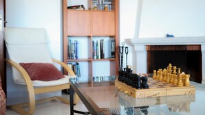 Una sala de estar con una mesa de centro de vidrio, una estantería de madera, una chimenea y un tablero de ajedrez.