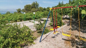 A playground with swings and a slide, surrounded by greenery and a view of the sea. - Holiday Home Blossom - Four Bedroom Holiday Home With Outdoor Pool and Jacuzzi - (Supetar)