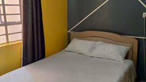 A bed with a white bedspread and two pillows, a window with a curtain, and a wall with a geometric design.