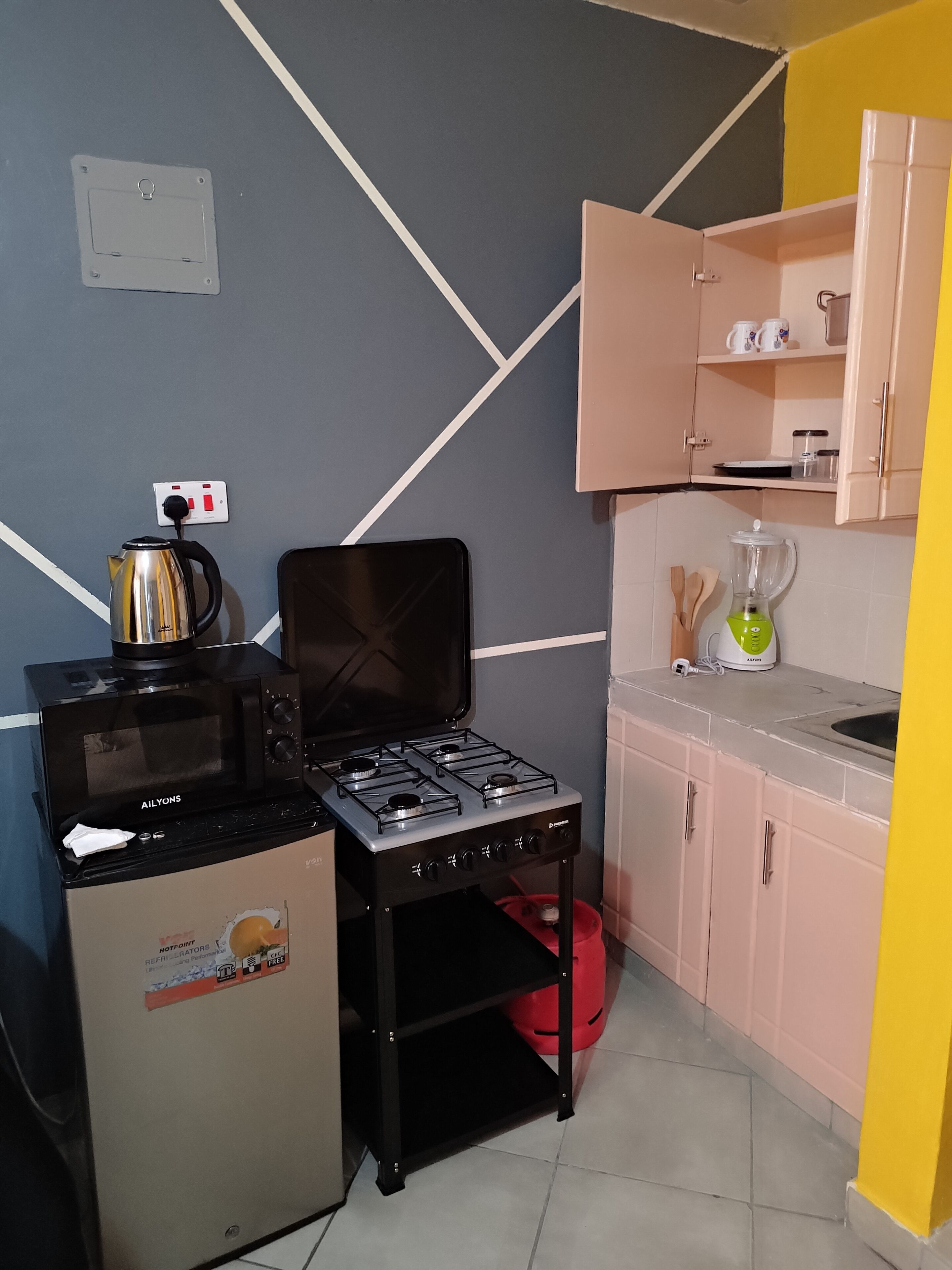 Eine kompakte Küchenzeile mit einem Gasherd, einer Mikrowelle, einem kleinen Kühlschrank und einem Mixer auf der Arbeitsfläche.