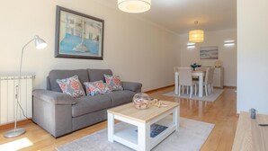 Una sala de estar moderna con un sofá gris, una mesita de centro blanca y un comedor con una mesa y sillas blancas.