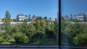 Vista desde una ventana que da a un parque con árboles y edificios al fondo.