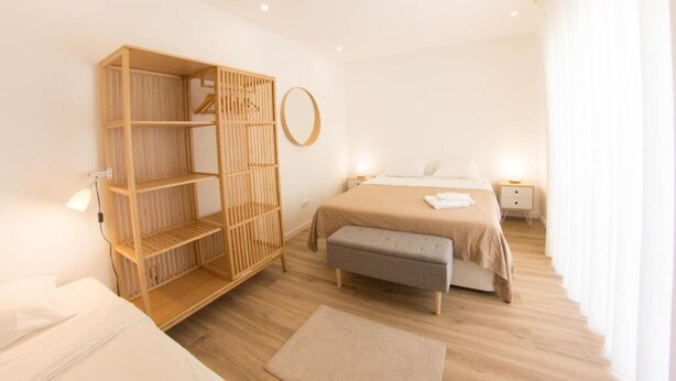 A modern bedroom with a wooden wardrobe, a bed with a grey bench, and a round mirror on the wall.