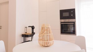 A modern kitchen with a built-in oven and microwave, a round table with a woven centerpiece, and a small side table with a coffee maker.