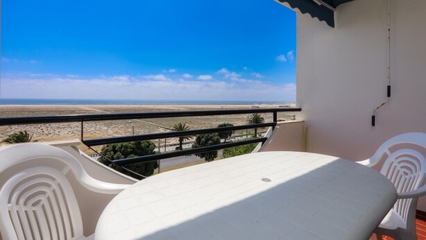 A balcony with a table and chairs, overlooking a beach and distant landscape. - Brasil Avenue by Rent4all (Figueira da Foz)