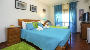 A hotel room with a large bed, a wooden dresser, a TV, and a window with curtains. - Brasil Avenue by Rent4all (Figueira da Foz)