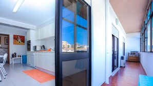 A modern kitchen with white cabinets, a large window, and a red-tiled floor. - Brasil Avenue by Rent4all (Figueira da Foz)