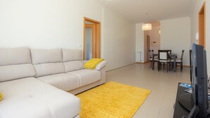 Una sala de estar moderna con un sofá, un tapete amarillo, una mesa de comedor con sillas y un televisor.