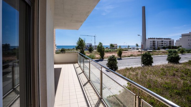 Un balcón con vistas despejadas al mar, una grúa de construcción y edificios modernos al fondo.