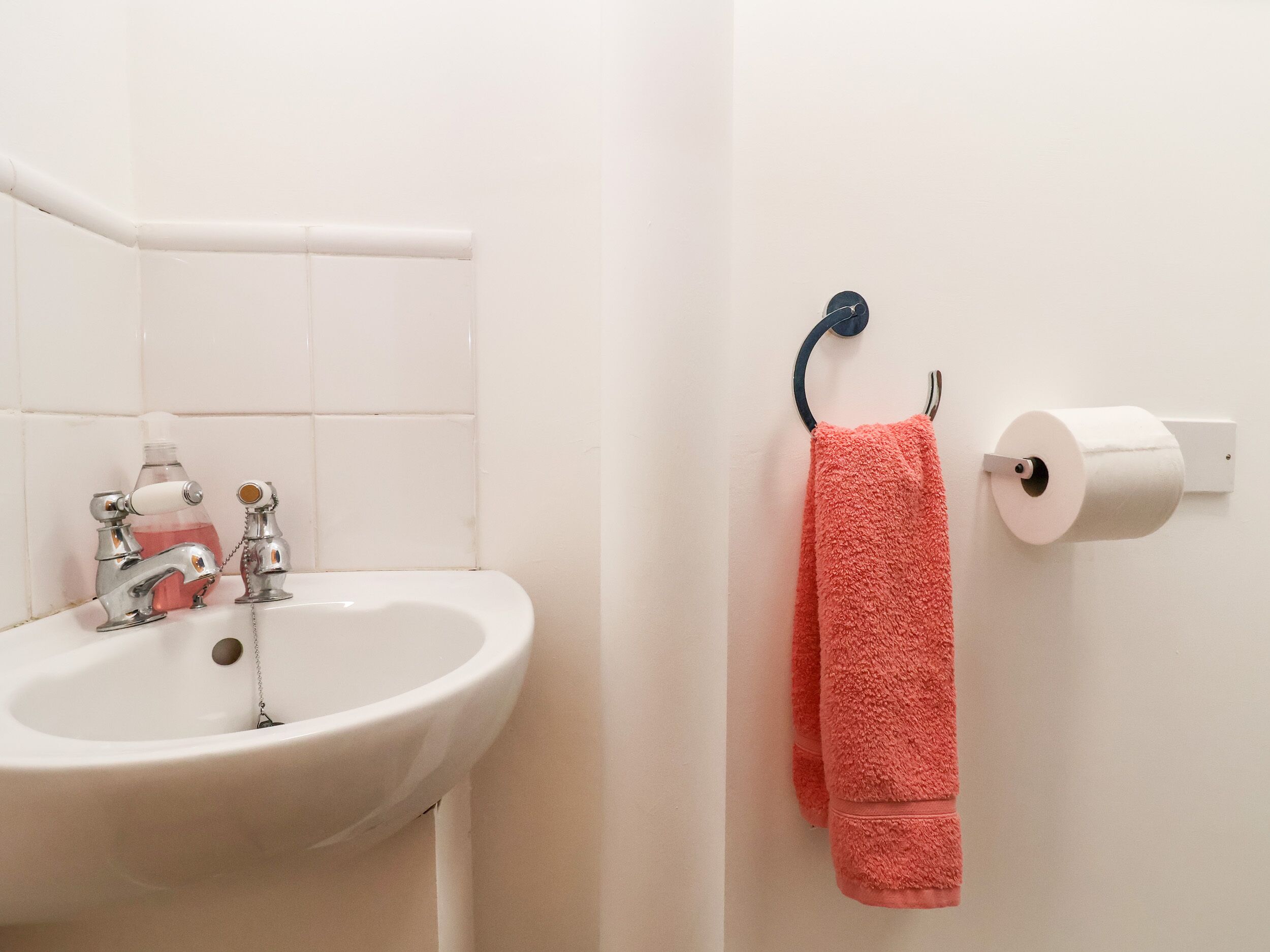 A bathroom with a white sink, a soap dispenser, and a towel rack with a pink towel.