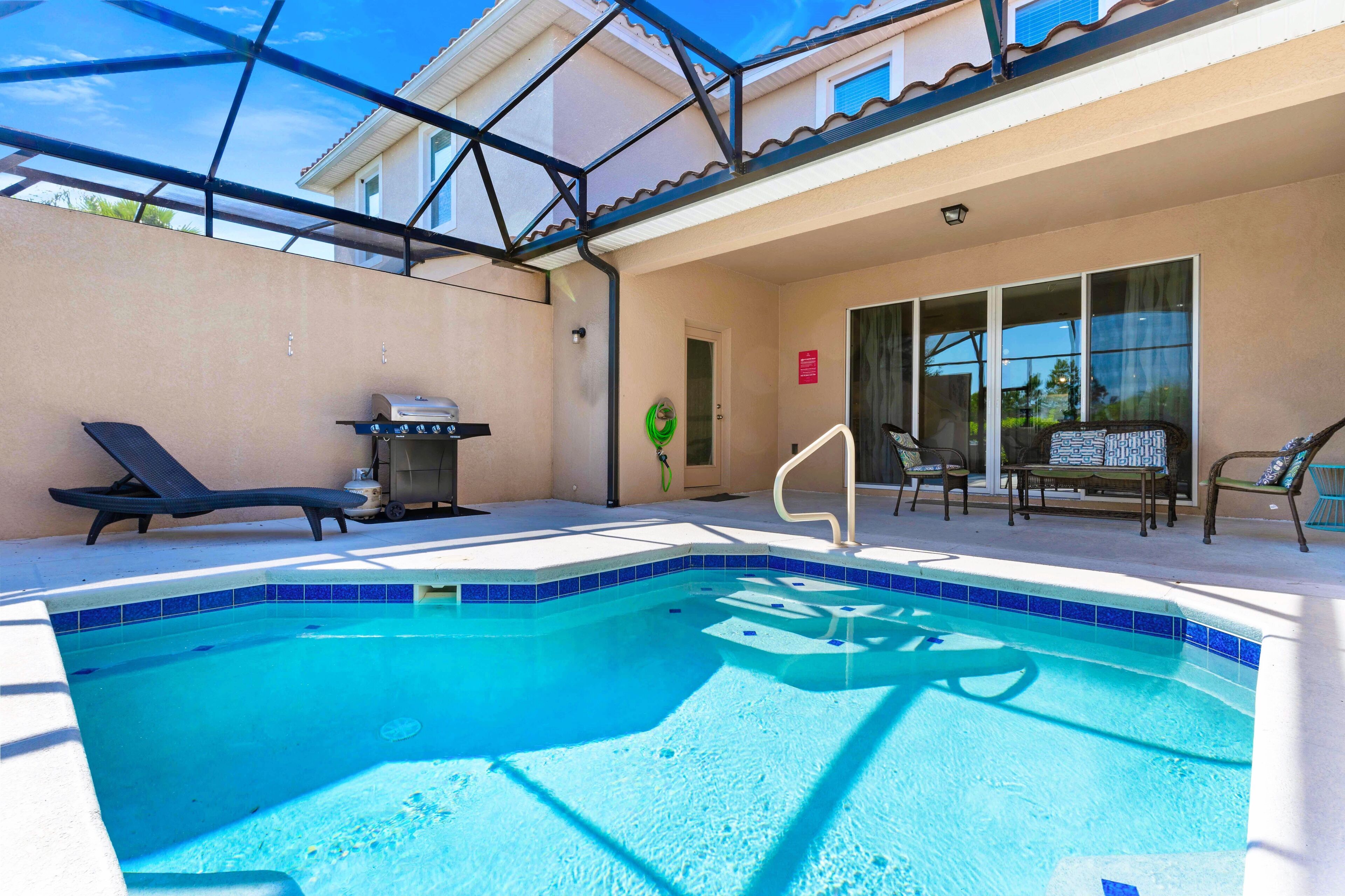 A swimming pool with a sunshade structure, lounge chairs, and a barbecue grill.