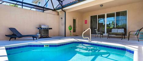 A swimming pool with a sunshade structure, lounge chairs, and a barbecue grill.