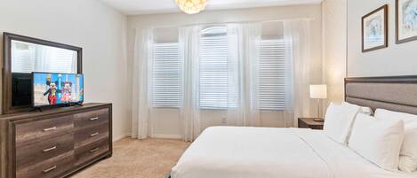 Un dormitorio con cama, cómoda, televisor y ventana con persianas.