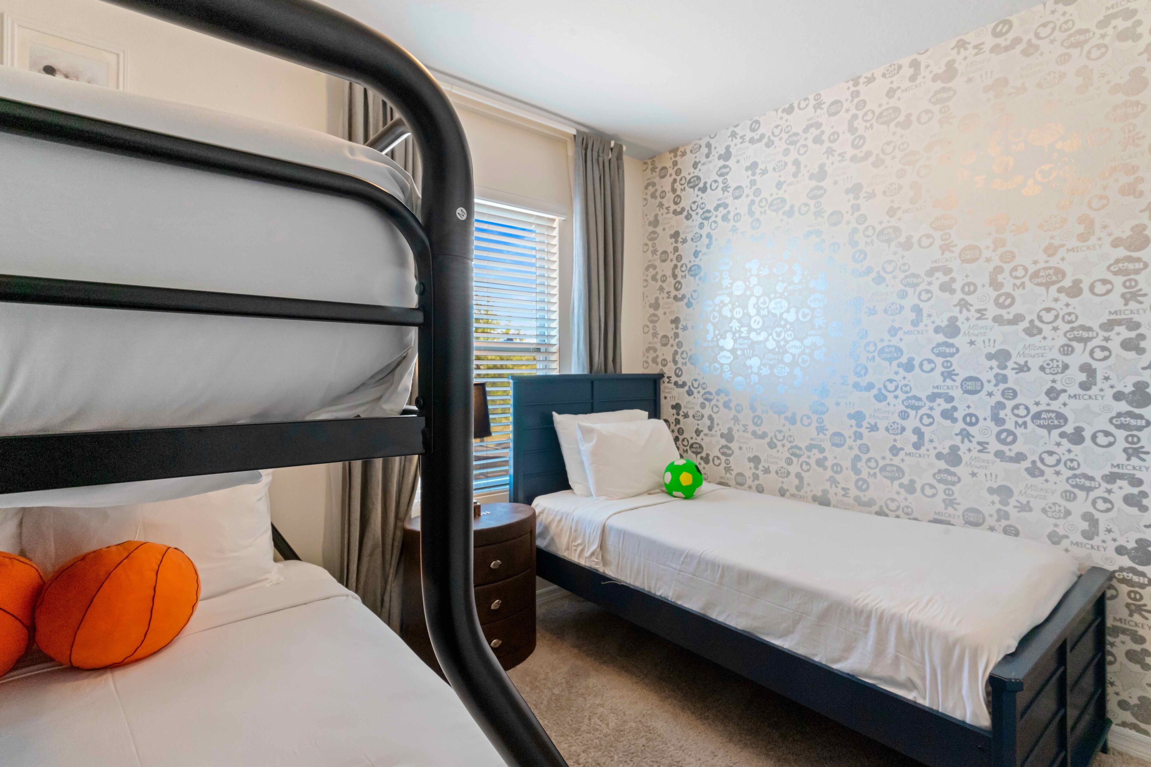 Un dormitorio con literas, una cama individual, una mesita de noche y un papel tapiz con temática de Mickey Mouse.