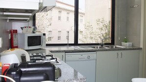 Cocina compacta con microondas, estufa y lavavajillas. Una ventana ofrece vistas a edificios y árboles.