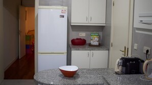 Una cocina compacta con armarios blancos, un refrigerador, un microondas y un tostador.