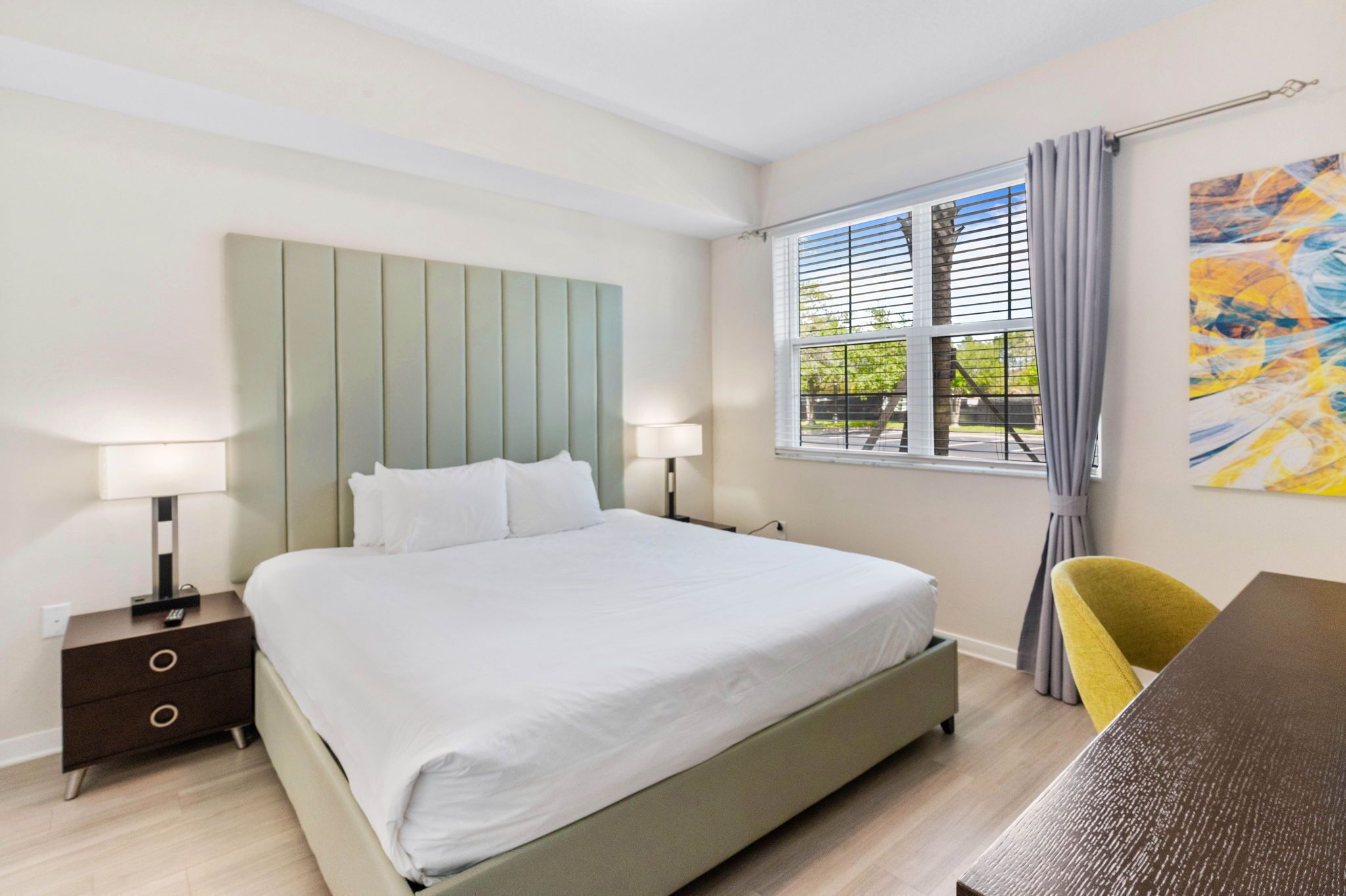 A hotel room with a bed, bedside tables, a desk, and a window with curtains.