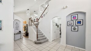 Um corredor amplo com escada, piso revestido em azulejo e quadros nas paredes.