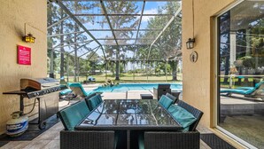 Um pátio externo com mesa, cadeiras, churrasqueira e piscina.