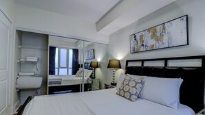 Una habitación de hotel con una cama grande, un armario, un escritorio con silla y una ventana con cortinas.