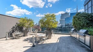 Una terraza en la azotea con mesas al aire libre, plantas en macetas y vistas del horizonte de la ciudad.