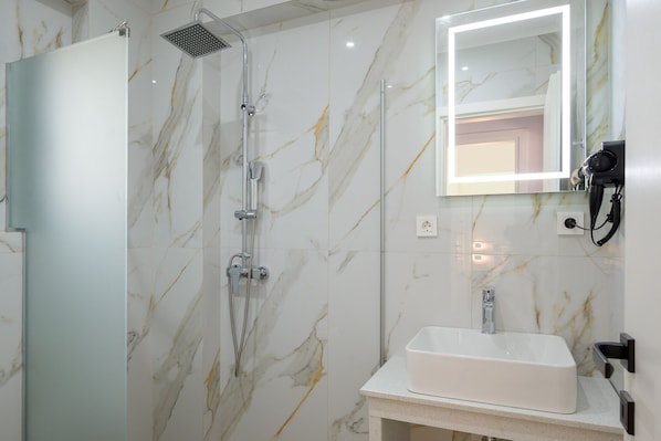 A modern bathroom with a marble wall, a shower, a sink, and a mirror with lights.