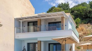 A two-story modern villa with a stone facade, a glass balcony, and a staircase leading to the upper level. - Vrachos Luxury Maisonettes (Parga)