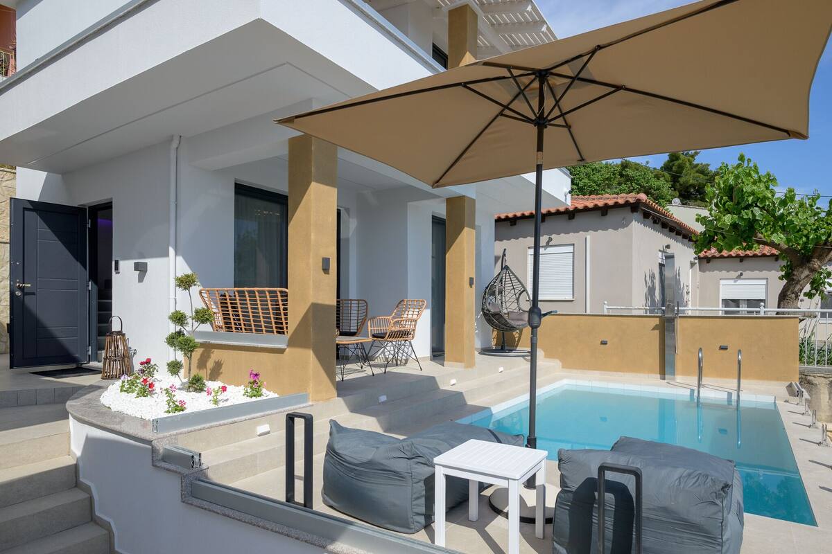 A modern outdoor pool area with a covered seating area, steps leading to the pool, and a door to the building.