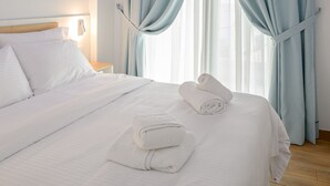 A hotel room with a large bed, light blue curtains, and a wooden ceiling. - Vrachos Luxury Maisonettes (Parga)